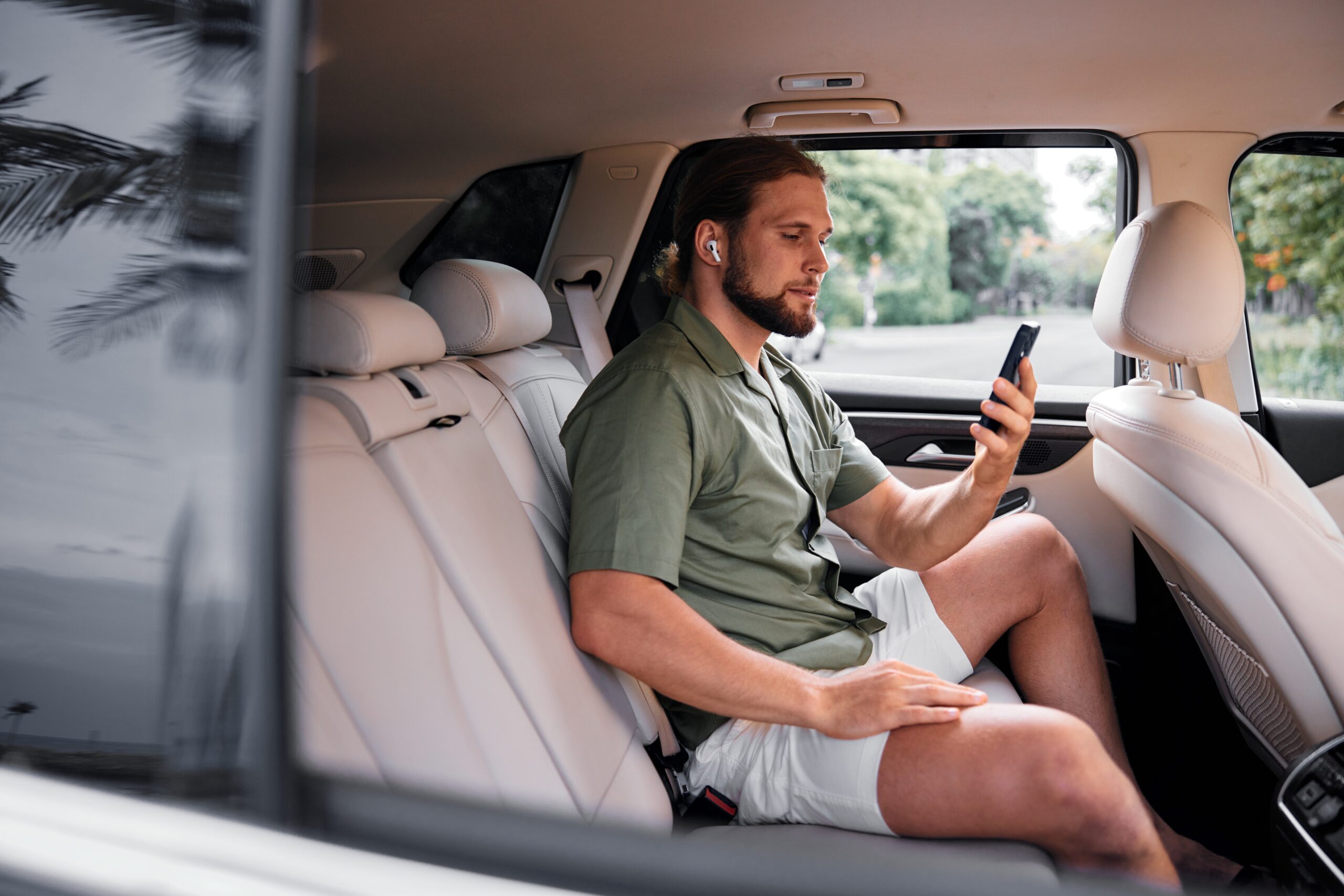 Man in shorts looking at phone while sitting in back seat of an Uber car.